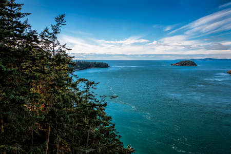 View of Deception Pass from the bridge with blue sky and water and foreground fall trees.の写真素材