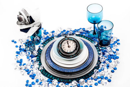 Table setting in the theme of new years eve with blue, and white. the centre piece of the setting is a large watch or clock set on one minute before midnight.の写真素材