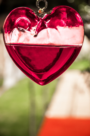 A glass heart with red liquid hanging from the ceiling with the walkway in the background.の写真素材