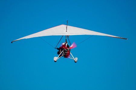 Ultralight aircraft from behind as it is taking of in to the blue skys, with pilot infront, and passanger right behind.の写真素材