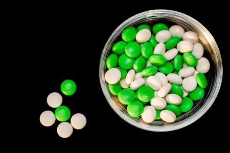 A glass bowl filled with white and green mints viewed from above while on a black background and five mints out, next to the bowl.の写真素材