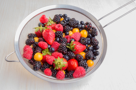 Mixed berries of different types, colors, and shapes in a colander.の写真素材