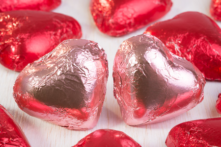 Two chocolate hearts, in pink wrapping foil, close together and surrounded by many other chocolate hearts in red wrapping foil.の写真素材