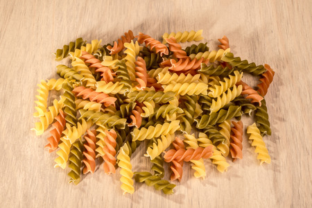 A small heap of three different colours of fussili ly on a wooden table.の写真素材