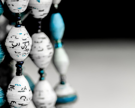 Necklaces made partly from paper beads in white and cyan, or light blue, hang from a display. の写真素材