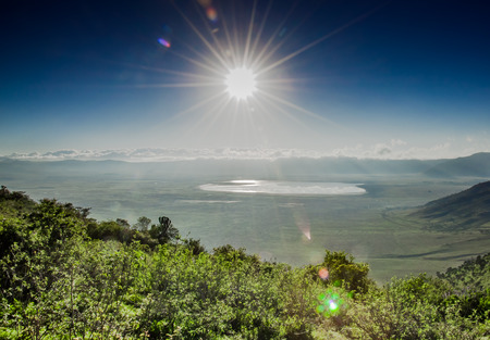 A view of the Ngorongoro Crater, with lake Magadi visbible in the distance infront of the clowds which cover the crater rim on the far side, as it is viewed in to the sun from the top of the crater rim.の写真素材