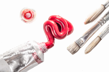 Permanent Rose oil paint squeezed from a tube near three paint brushes and the lid of the tube on an isolated white background as viewed from directly above.の写真素材