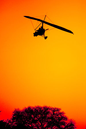 The silhouette of an ultra light aircraft on final approach as it comes in for landing against the...