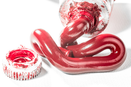 Red oil paint called Permanent Alizarin Crimson,  is squeezed from a tube on to a white canvas next to the lid of the tube.の写真素材