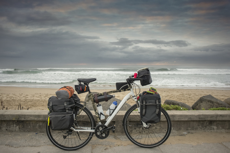 A long distance bicycle stand parked against a low wall next to the road with the ocean in the backgroundの写真素材