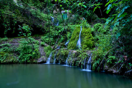 nice picture of a fountain pouring water from a wall forming a small lakeの写真素材