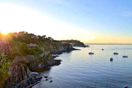 Collioure coastline at sunset with boats sailing on a calm Mediterranean seaの写真素材