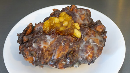 An upclose view of an apple fritter served on a white plate