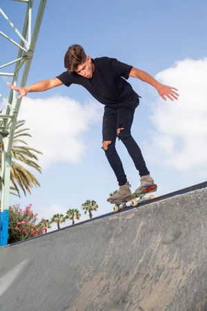 Young skateboarder performing tricks in a park, with street background and blue sky.