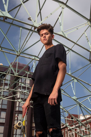 Portrait of young skateboarder with black t-shirt and street and blue sky background.の写真素材