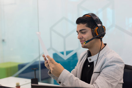 Young man smiling with headphones, reading a document in coworking office.の写真素材