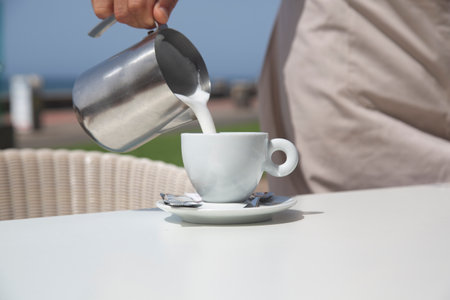 Hand serving milk into coffee cup with blue sky background.の写真素材