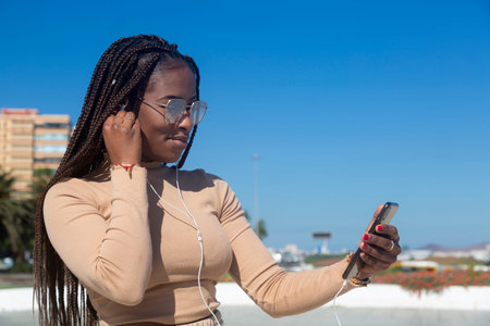 Young black afro woman smiling looking at her cellphone, outdoors with blue sky and sea background....