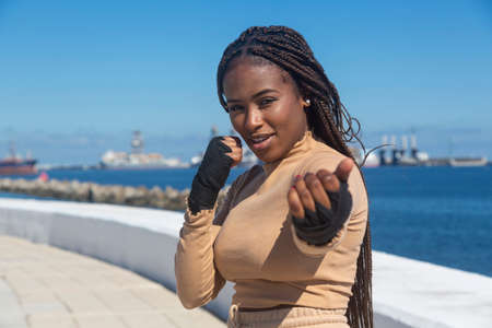 Portrait of beautiful young afro american woman looking at camera, with bandages on her hands to practice martial arts, boxing. Sky and sea background, seafront.の写真素材