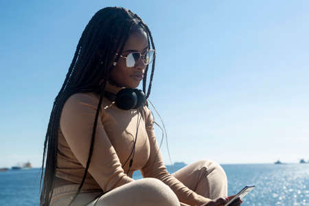 Young black woman looking at her cellphone with headphonesの写真素材