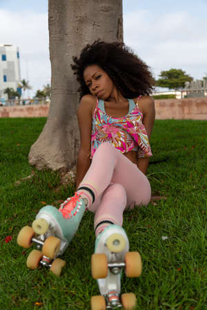 beautiful young afro woman with roller skates sitting on the grassの写真素材