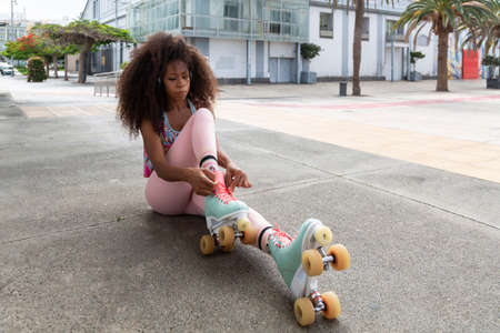Afro skater woman seated tying her skatesの写真素材