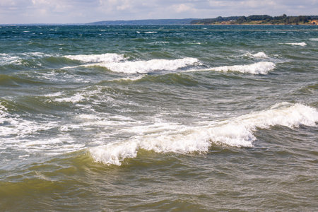 The Beach of Juelsminde in Denmark. View along the coastline and of the stormy Baltic Sea. Waves crash on the beach.の写真素材