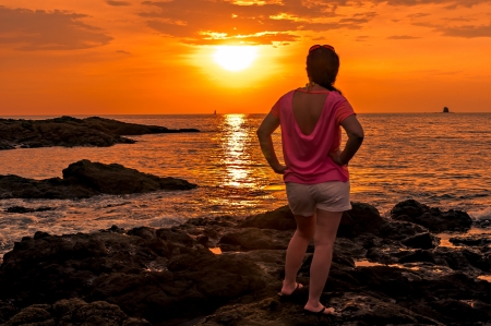 woman standing on the rocks watching the sunsetの写真素材