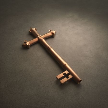 An old fashioned brass key laying on white surface shaped like a crossの写真素材