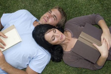 Attractive, young couple lying in the grass with booksの写真素材