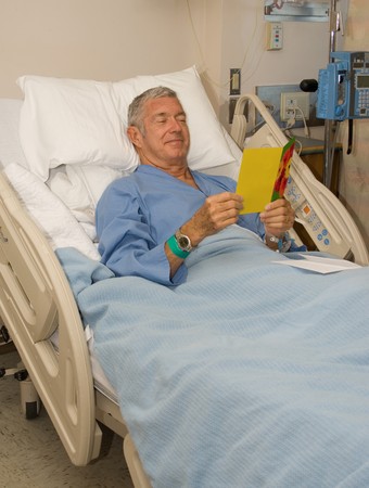 Man in hospital bed reading a get well cardの写真素材