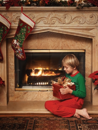 8 year old boy sitting beside the fireplace with a wrapped Christmas gift in his lapの写真素材