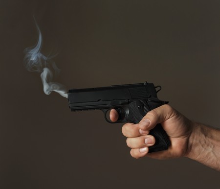 hand holding smoking pistol on dark backgroundの写真素材
