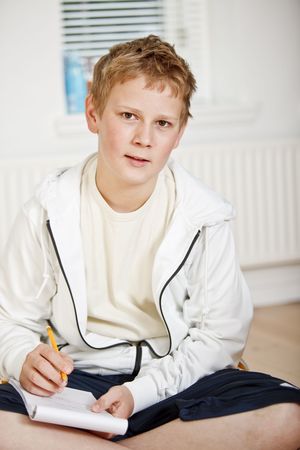 Boy sitting on the flloor in his bedroom doing homeworkの写真素材