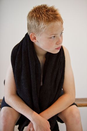 Young boy sitting on a bench with a towel around his neckの写真素材