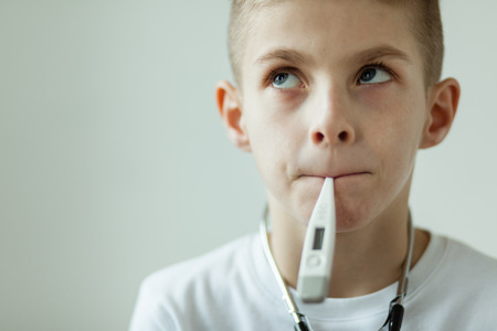 Close up Thoughtful White Boy with Digital Thermometer in his Mouth Looking up Seriously Against White Wall Background.の写真素材