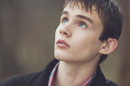 Close up of teenaged boy in jacket looking upward with an expression of concern or amazementの写真素材