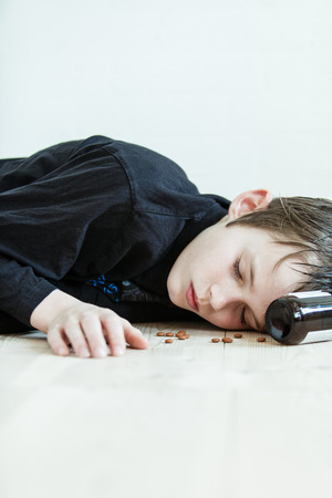 Young boy lying dead on the floor after committing suicide with a bottle of prescription drugs with tablets scattered around his face and the empty bottle at his headの写真素材