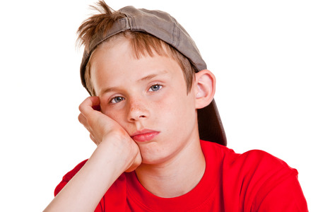 Bored depressed young boy with sad lonely eyes resting his chin on his hand looking at the camera with a doleful expressionの写真素材
