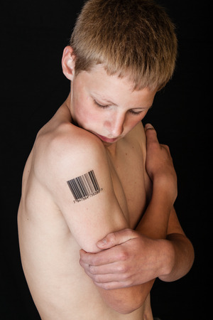 One shirtless boy with short brown hair and bar code stamped on his bare arm against a black backgroundの写真素材