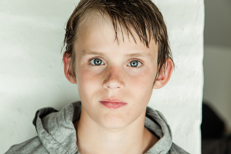 Handsome young boy with wet hair in a grey hoodie looming directly into the camera with a serious expression, close up head shotの写真素材