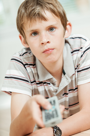 Attractive young boy using a remote control pointing it at the camera, focus to his face with a serious intent expressionの写真素材