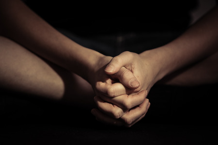 Close up front view on pair of folded hands over crossed legs in sitting position with dark backgroundの写真素材
