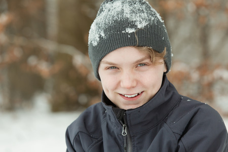 Smiling happy young boy with a head covered in snow snuggling down in his warm jacket as he plays outdoors on a cold snowy winter day, with copy spaceの写真素材