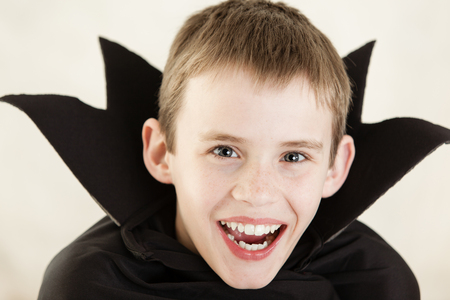 Single cute little laughing boy dressed in black vampire cloak over white backgroundの写真素材