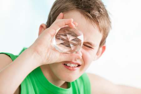 Boy wearing sleeveless green shirt holds a multi faceted crystal against his eye and squintsの写真素材