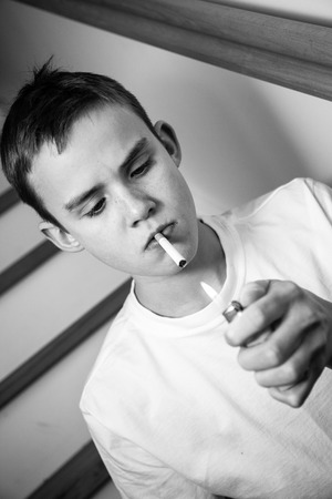 Experimental tilted black and white image of boy lighting cigarette while standing in stairwellの写真素材