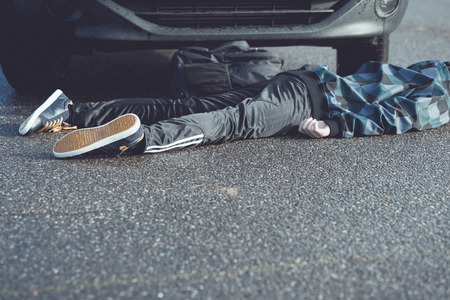 Close Up of Unrecognizable Car Accident Fatality - Bottom Half and Legs of Young Teenage Boy Car Accident Victim Lying on Wet Road Pavement in front of Stopped Vehicleの写真素材