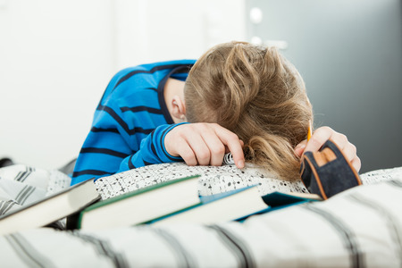 Exhausted young boy asleep on his text books under stress from his studying as he sits on his bed at home doing homeworkの写真素材