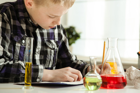 Diligent young boy doing his science homework writing notes as he sits at home with an array of lab glassware filled with colorful solutionsの写真素材